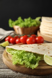 Photo of Tasty homemade tortilla, lettuce, lime and tomatoes on wooden table