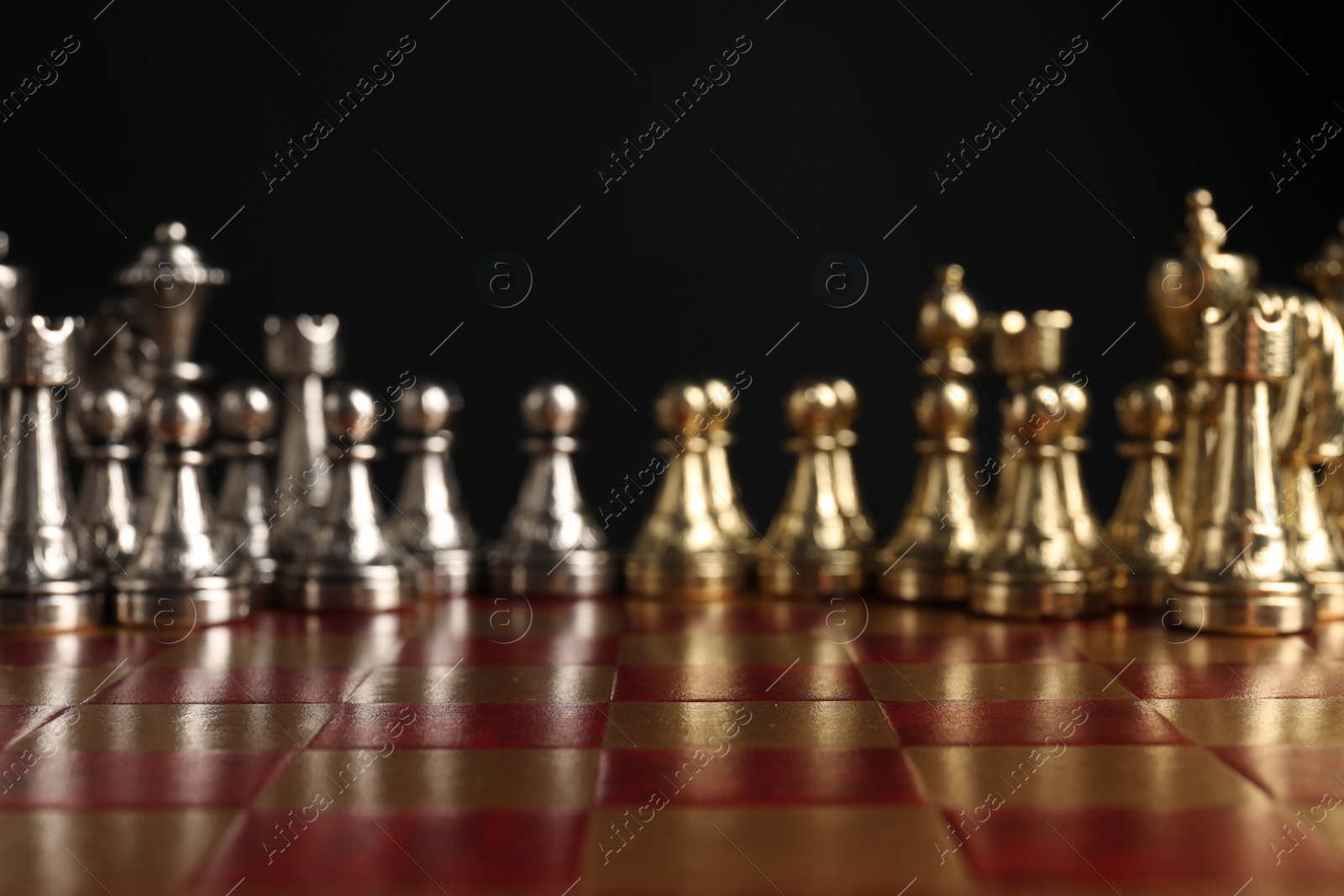 Photo of Many chess pieces on wooden checkerboard against black background, selective focus