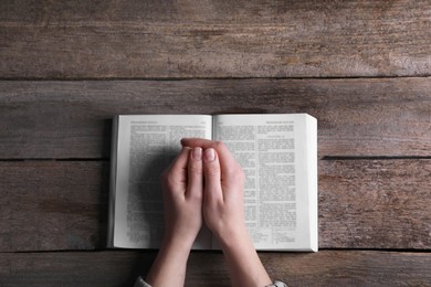 Photo of Religion. Christian woman praying over Bible at wooden table, top view