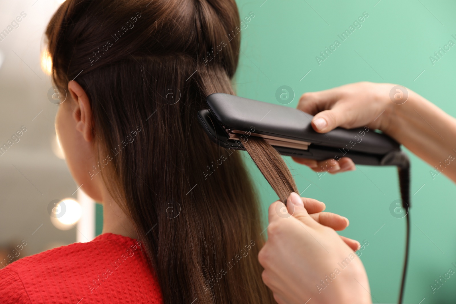 Photo of Stylist straightening woman's hair with flat iron in salon