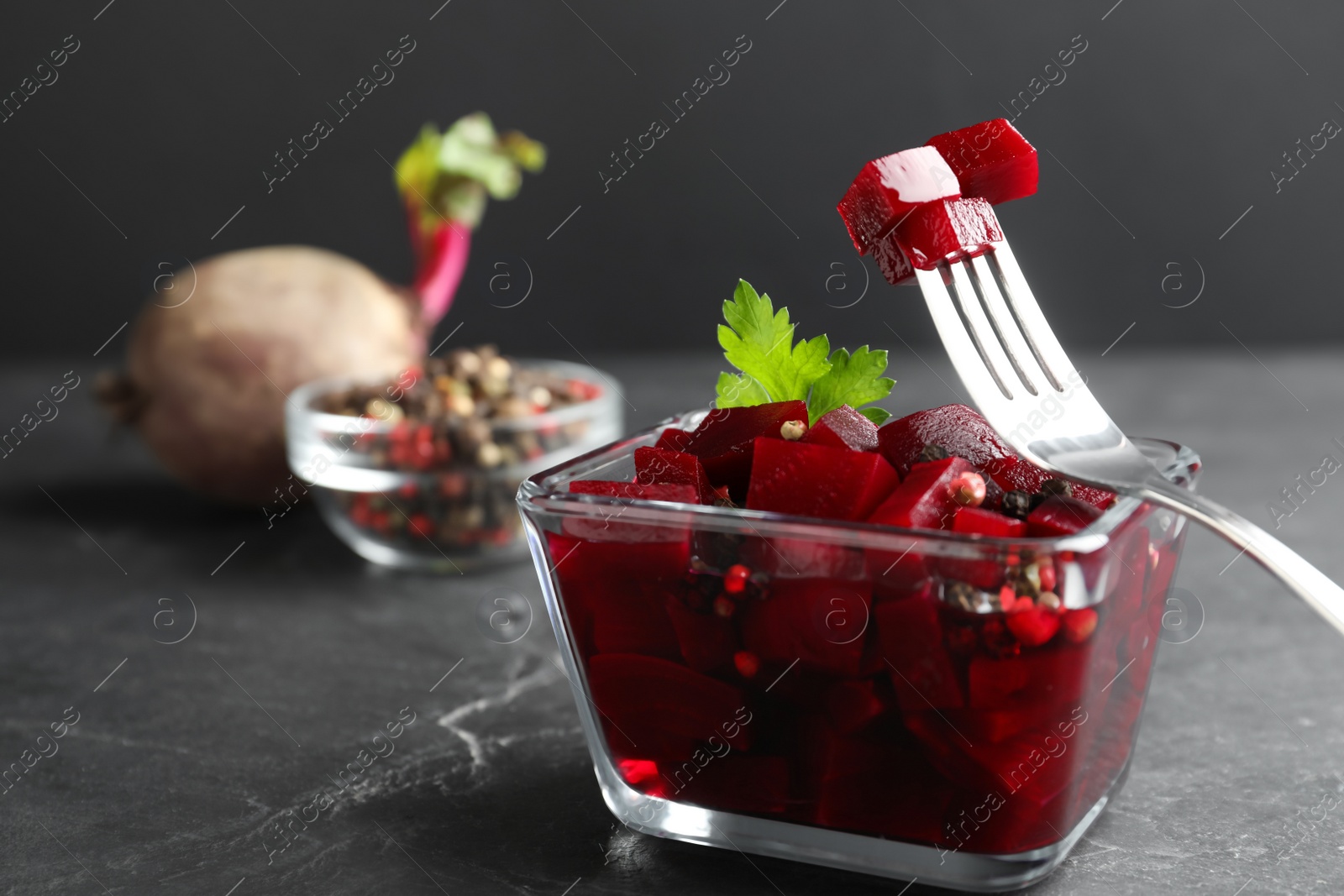 Photo of Pickled beets and fork over glass bowl on dark marble table