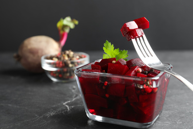 Pickled beets and fork over glass bowl on dark marble table