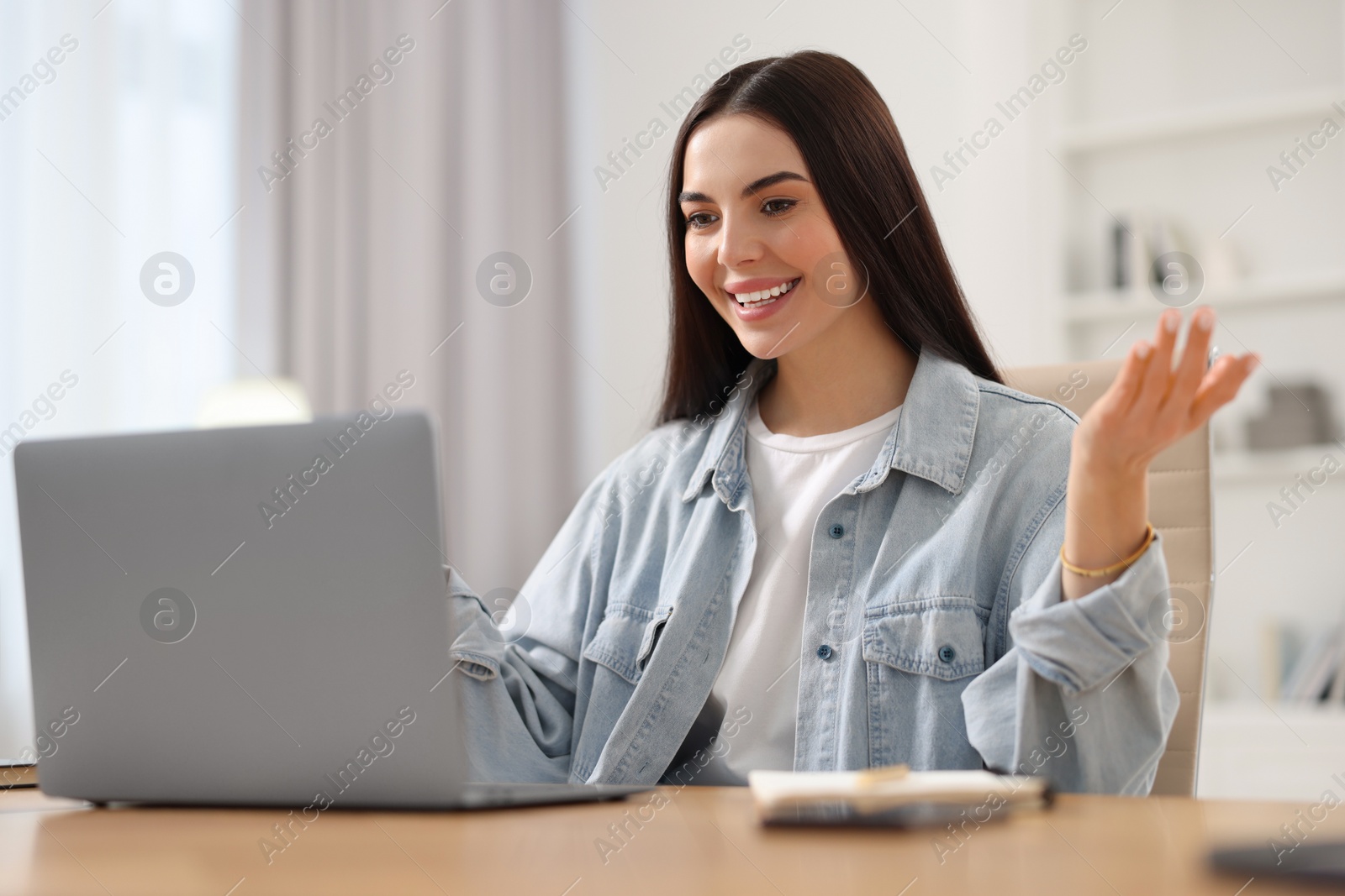 Photo of Young woman using video chat during webinar at table in room