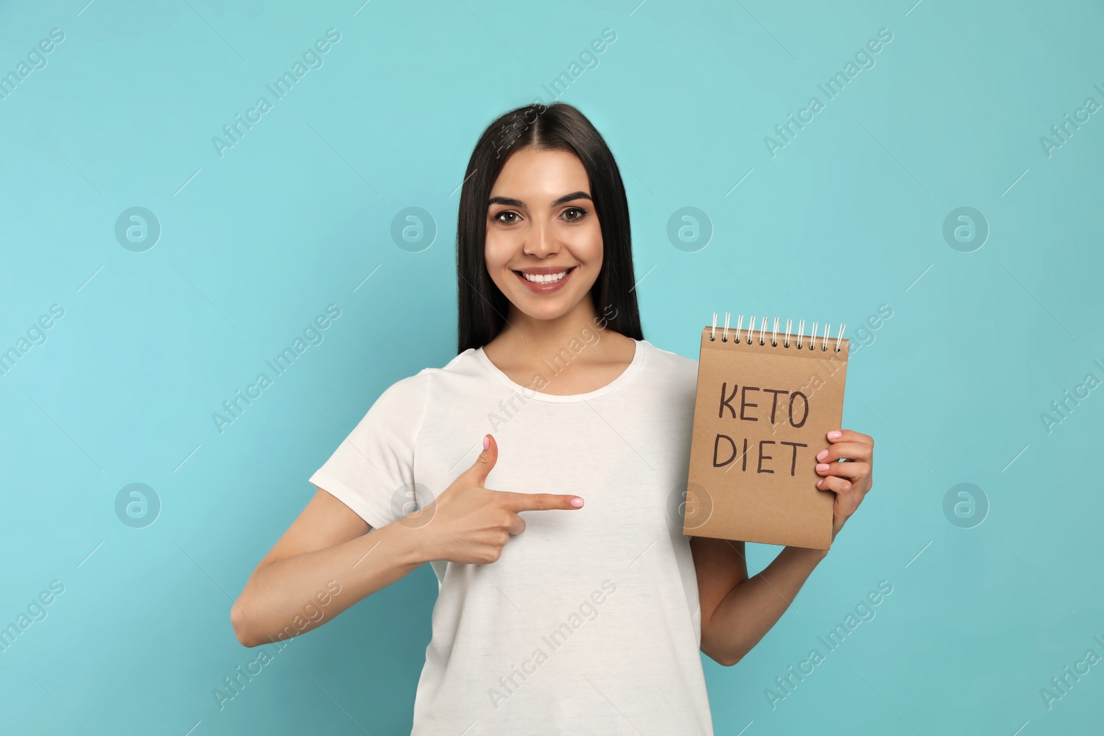 Photo of Happy woman holding notebook with words Keto Diet on turquoise background