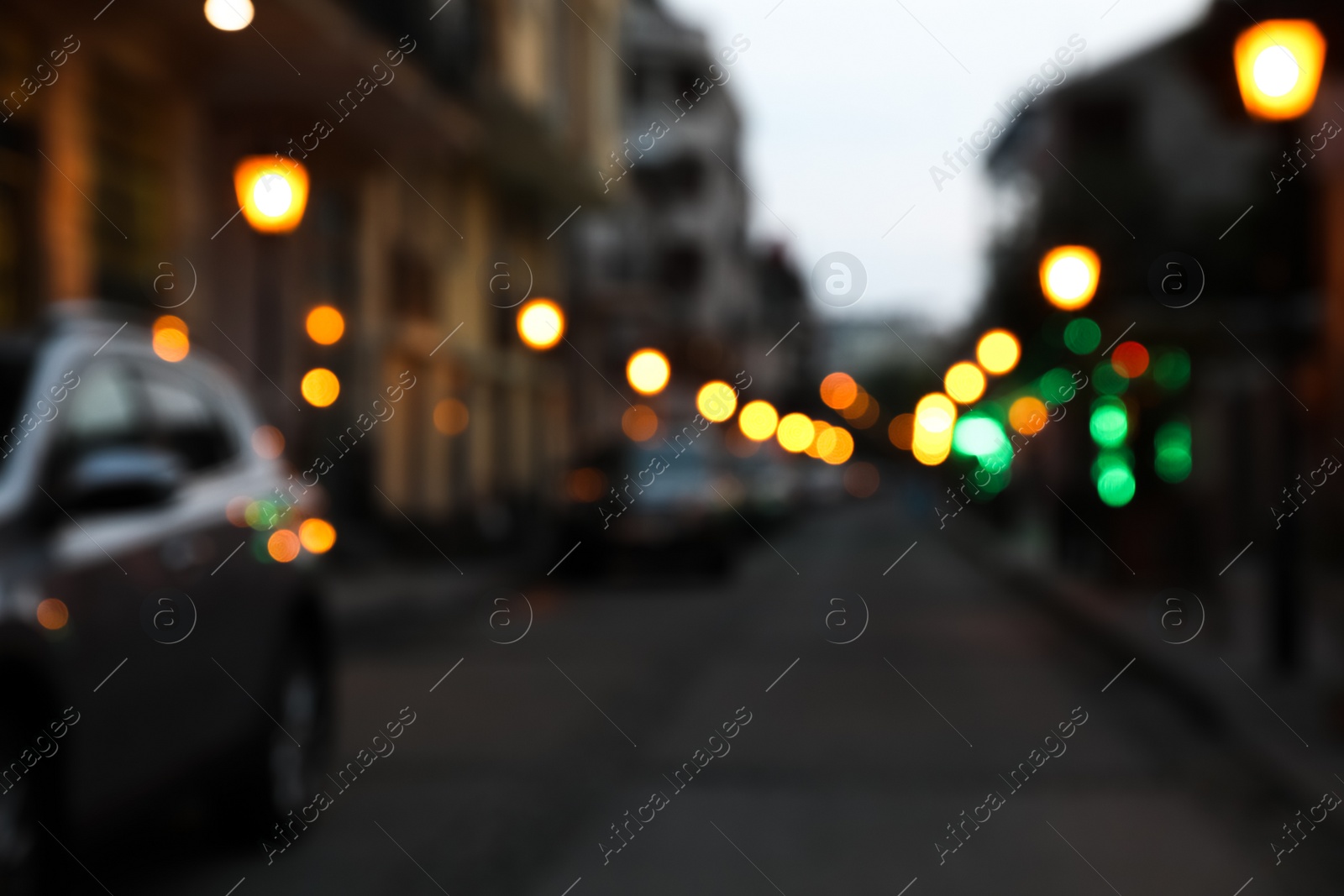 Photo of Blurred view of city street with parked cars in evening