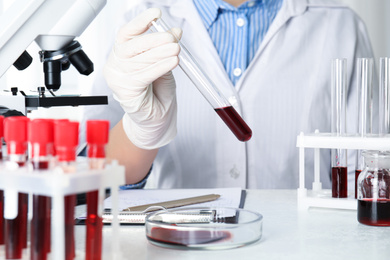 Photo of Scientist holding test tube with blood sample in laboratory, closeup. Virus research