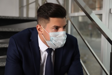 Photo of Sad man in protective mask on stairs indoors. Self-isolation during coronavirus pandemic