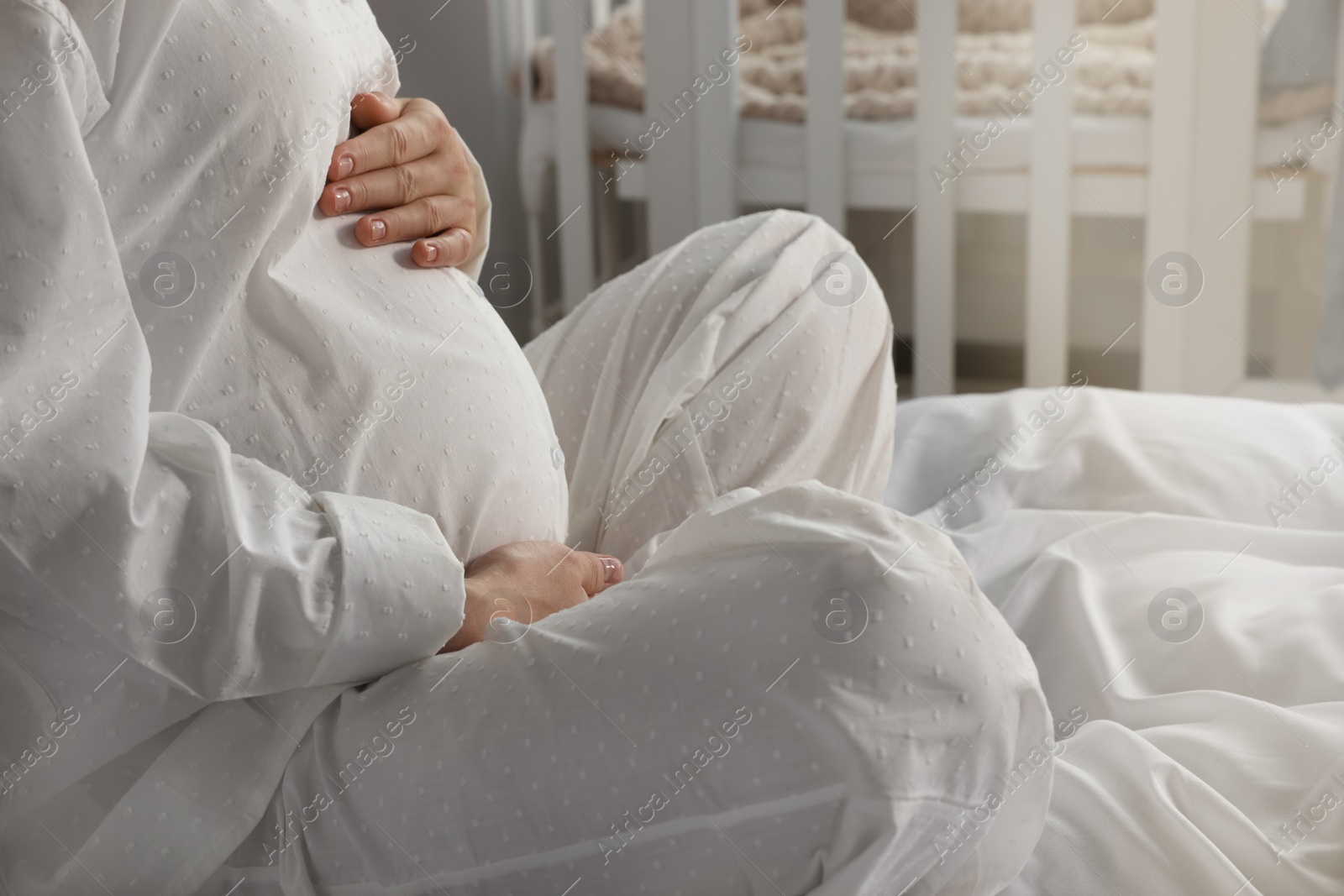 Photo of Pregnant woman in pajamas on bed at home, closeup