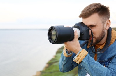 Male photographer taking picture of beautiful landscape with professional camera on green hill. Space for text