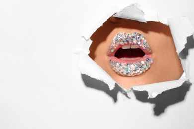 Photo of View of beautiful young woman with creative lips makeup through hole in color paper