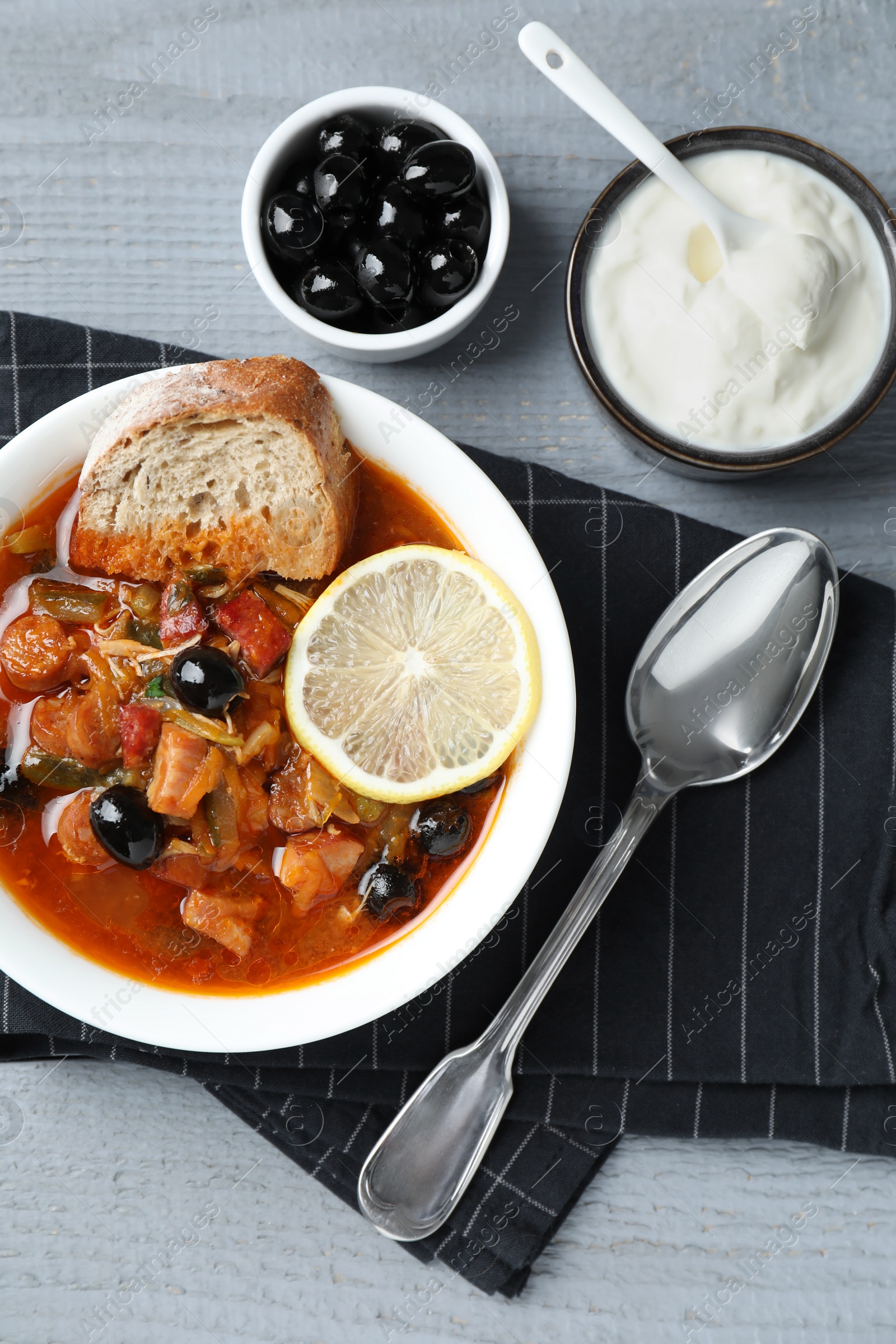 Photo of Meat solyanka soup with sausages, olives and vegetables served on grey wooden table, flat lay