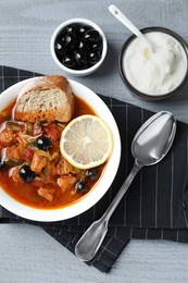 Photo of Meat solyanka soup with sausages, olives and vegetables served on grey wooden table, flat lay