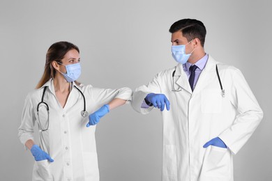 Doctors greeting each other by bumping elbows instead of handshake on light grey background