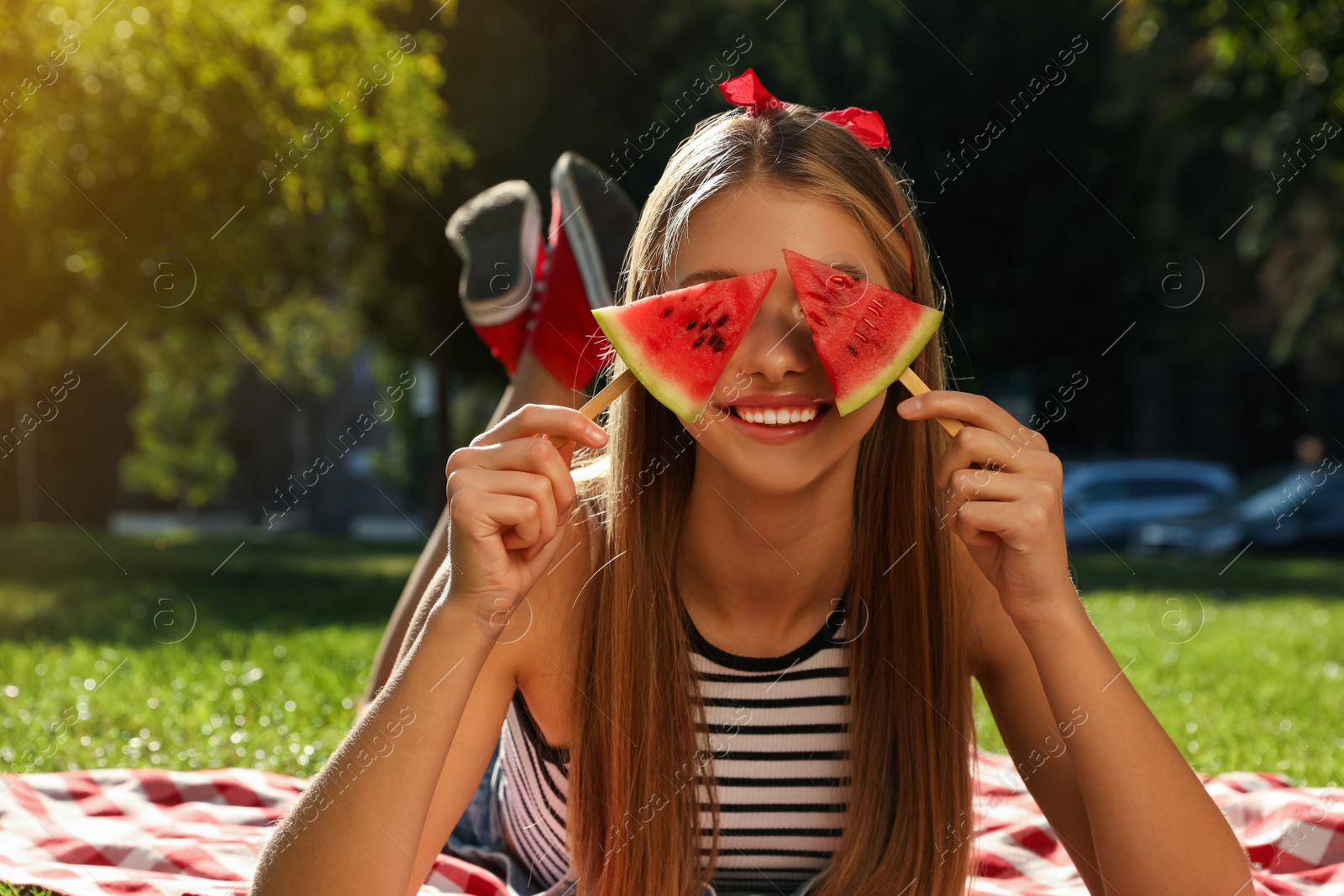 Photo of Beautiful girl with pieces of watermelon on picnic blanket in park