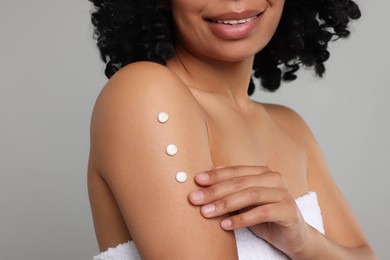 Photo of Young woman applying body cream onto arm on grey background, closeup