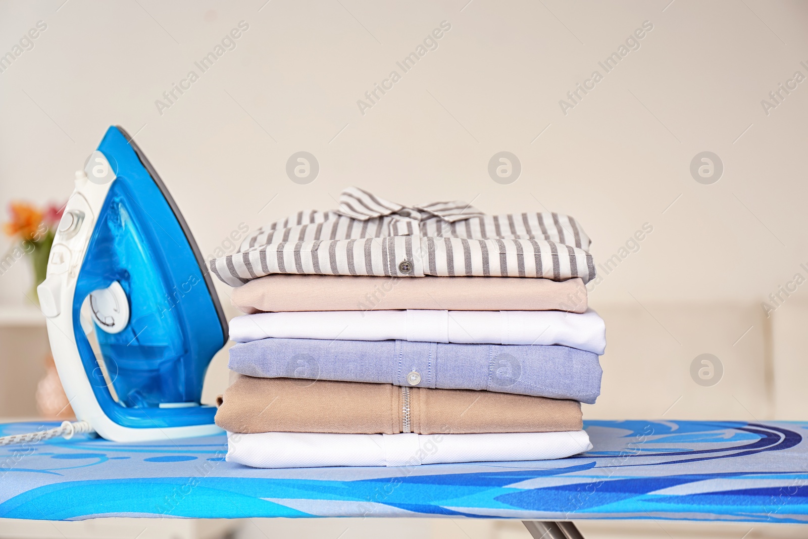 Photo of Stack of clean clothes and iron on board indoors