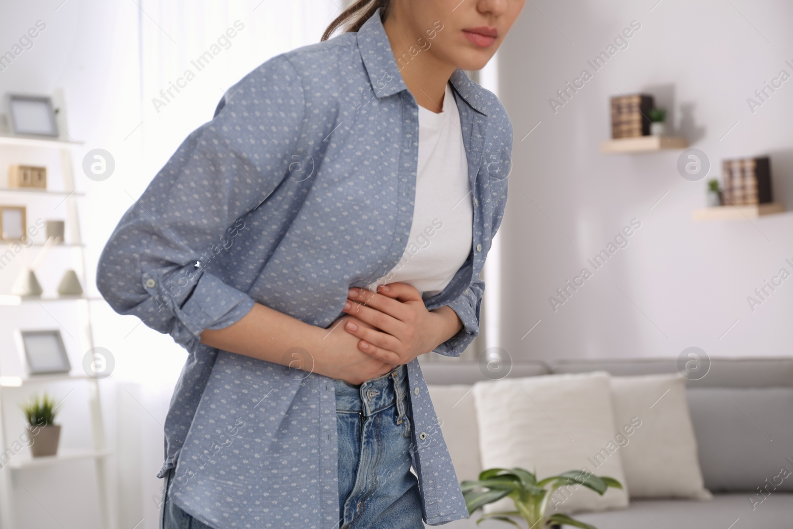 Photo of Young woman suffering from stomach ache at home, closeup. Food poisoning