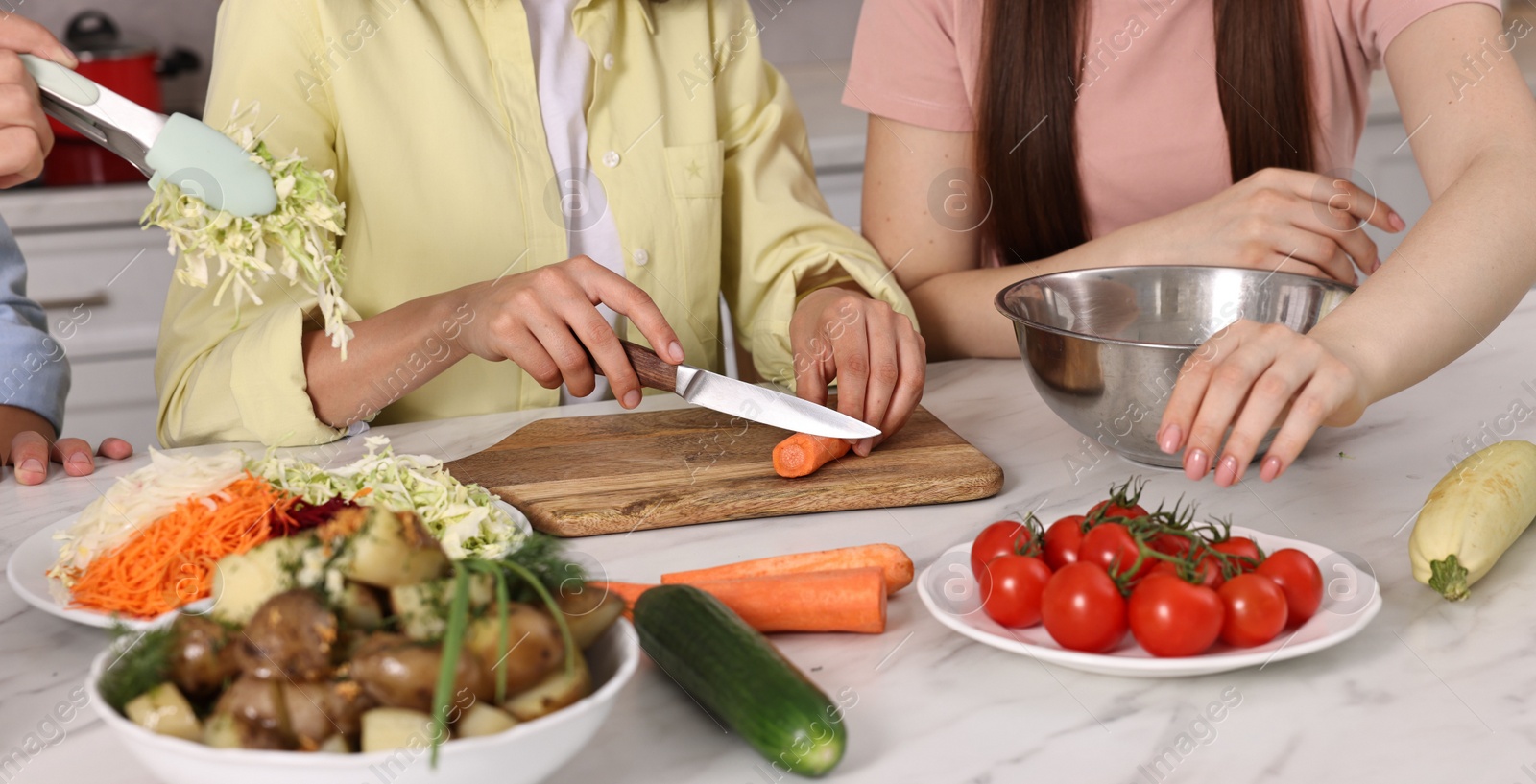 Photo of Friends cooking healthy vegetarian meal at white marble table in kitchen, closeup