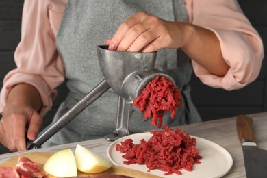 Photo of Woman making beef mince with manual meat grinder at light wooden table, closeup