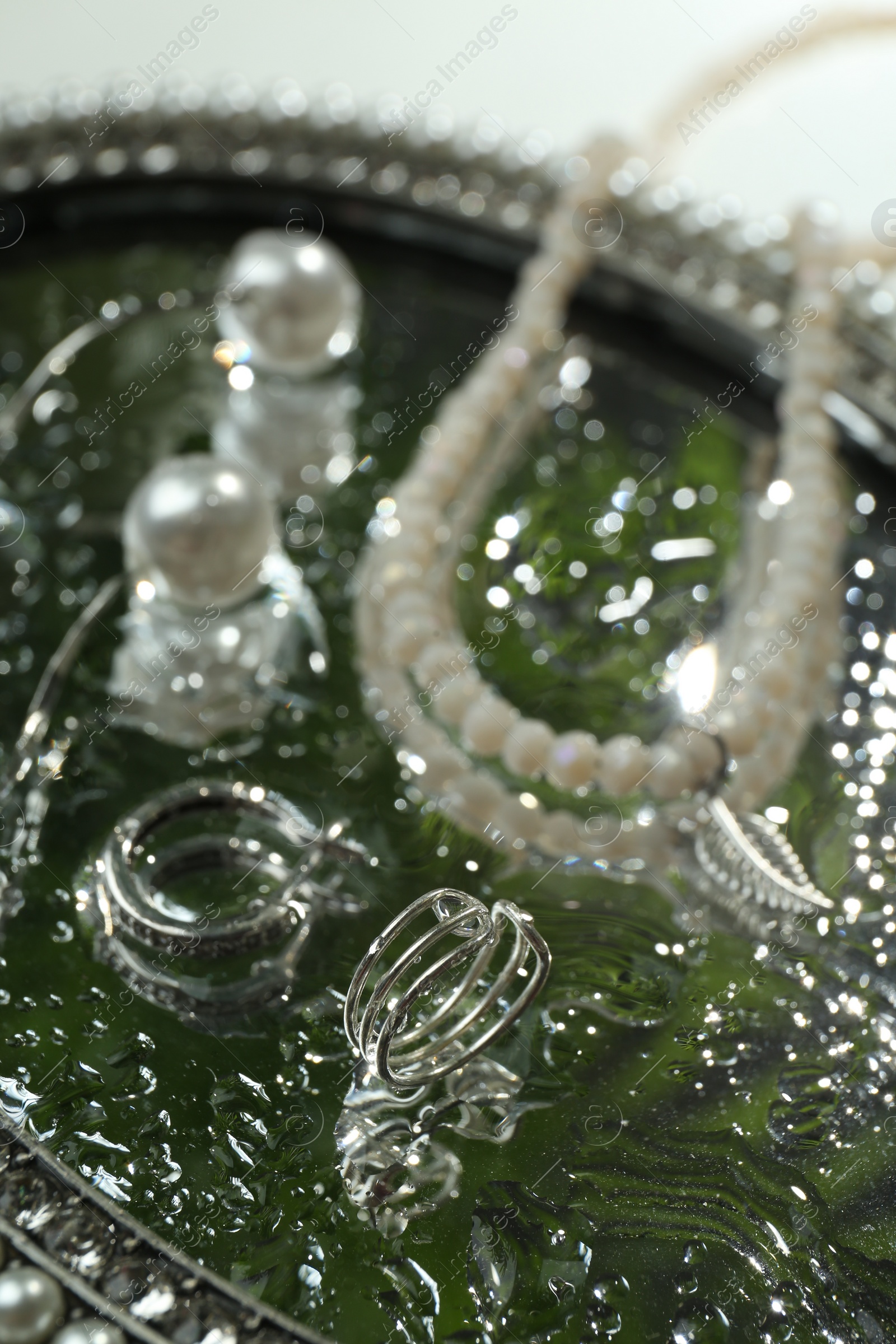 Photo of Elegant jewelry with water drops on vintage mirror, closeup