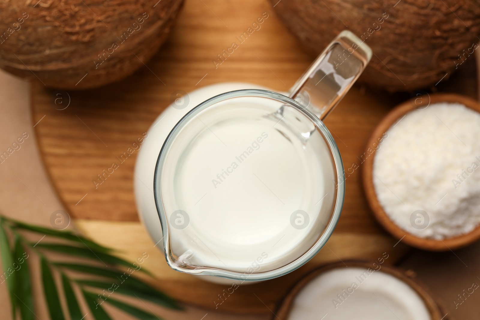 Photo of Glass jug of delicious vegan milk, coconuts and leaf on brown background, flat lay