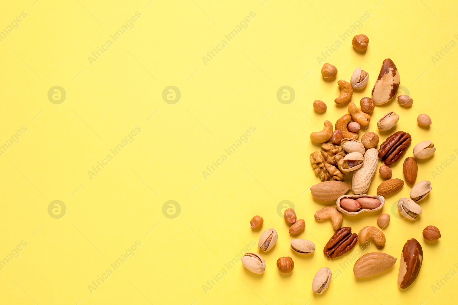 Photo of Different delicious nuts on yellow background, flat lay. Space for text