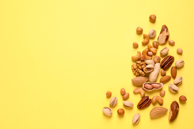 Different delicious nuts on yellow background, flat lay. Space for text