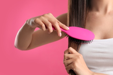 Woman with hair brush on color background, closeup