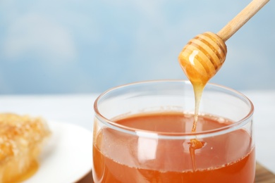 Photo of Sweet honey dripping from dipper into glass jar, closeup