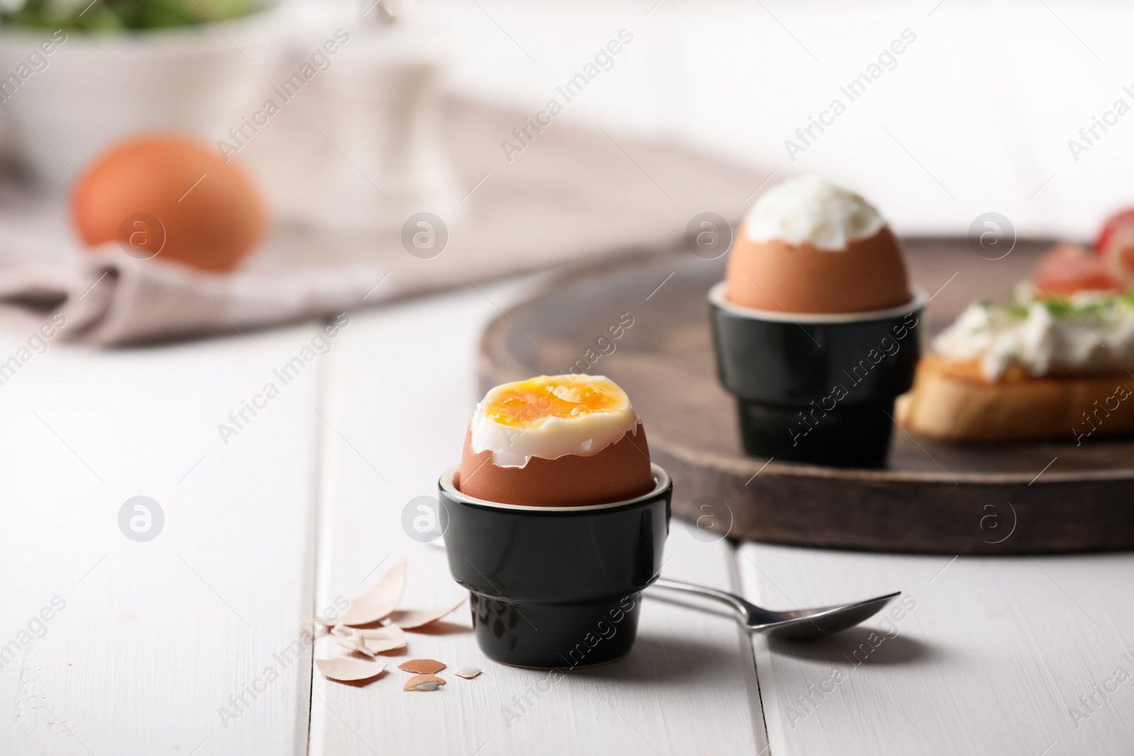 Photo of Fresh soft boiled egg in cup served on white wooden table. Space for text