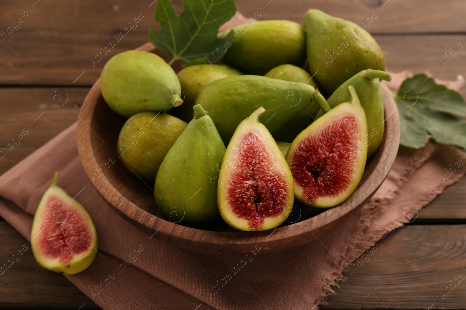 Photo of Cut and whole green figs in bowl on wooden table, closeup
