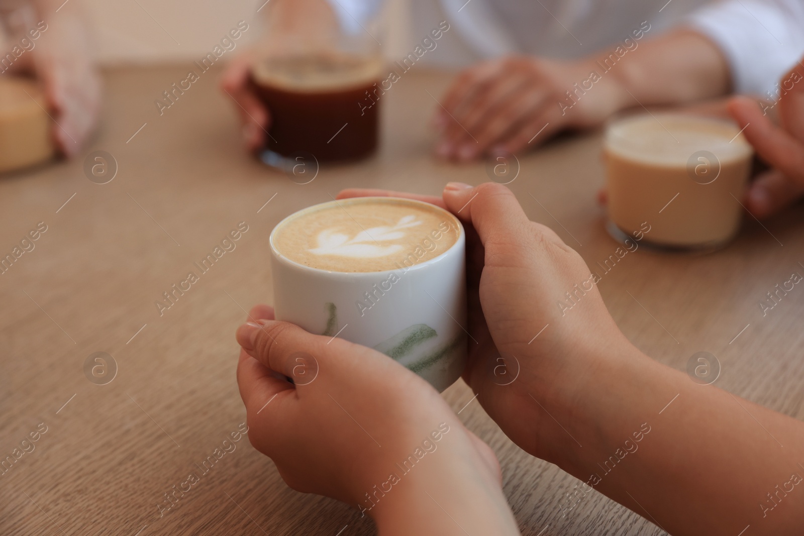 Photo of Woman holding cup of coffee spending time with friends in cafe, closeup