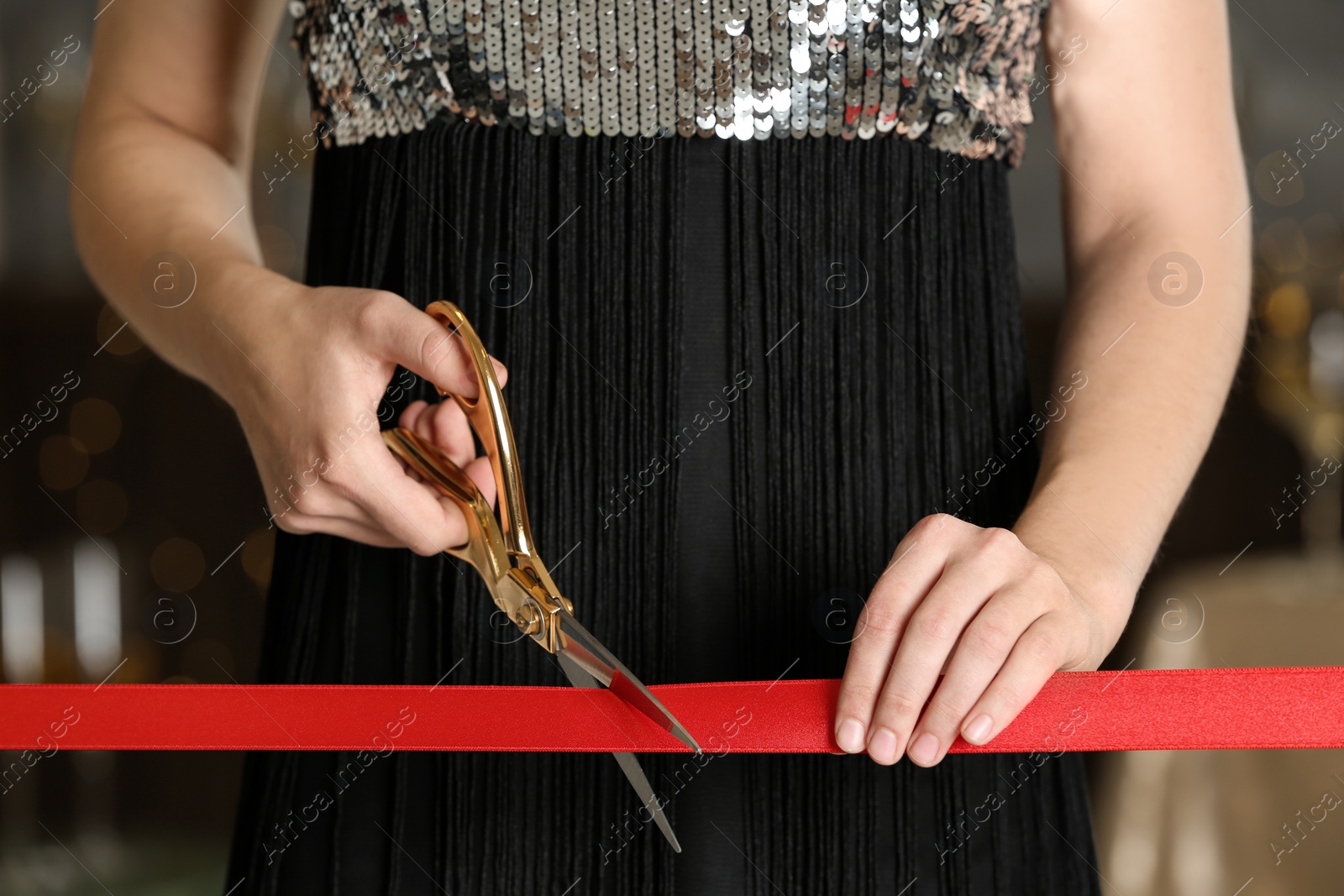 Photo of Woman cutting red ribbon with scissors indoors at ceremonial event