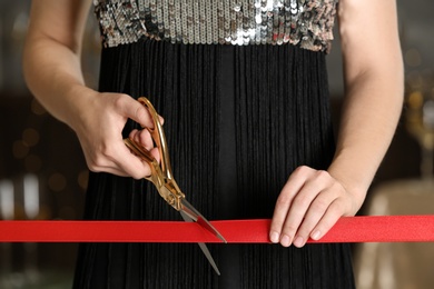 Photo of Woman cutting red ribbon with scissors indoors at ceremonial event