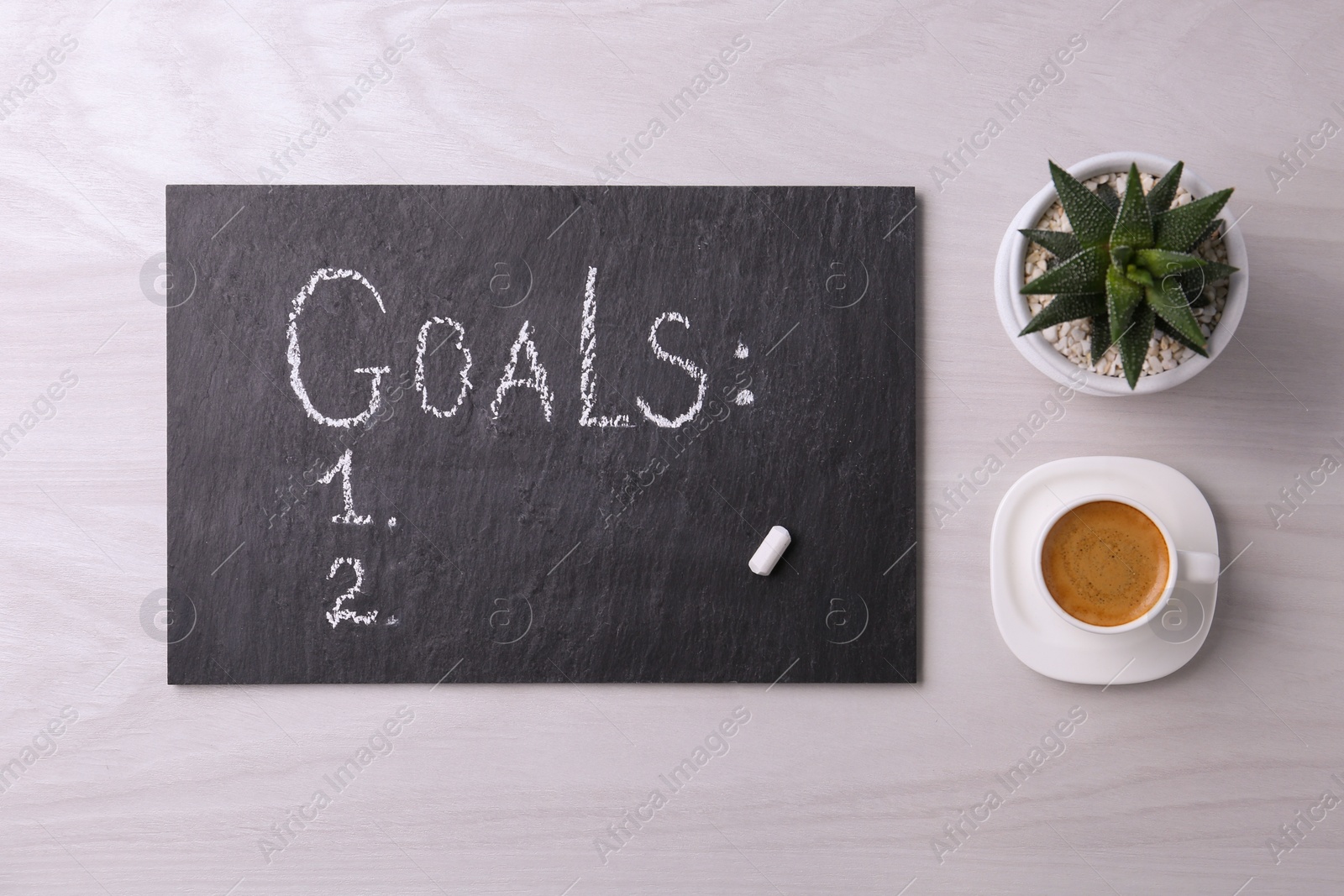 Photo of Slate board with word Goals, numbering, houseplant and cup of coffee on white wooden table, flat lay. Planning concept