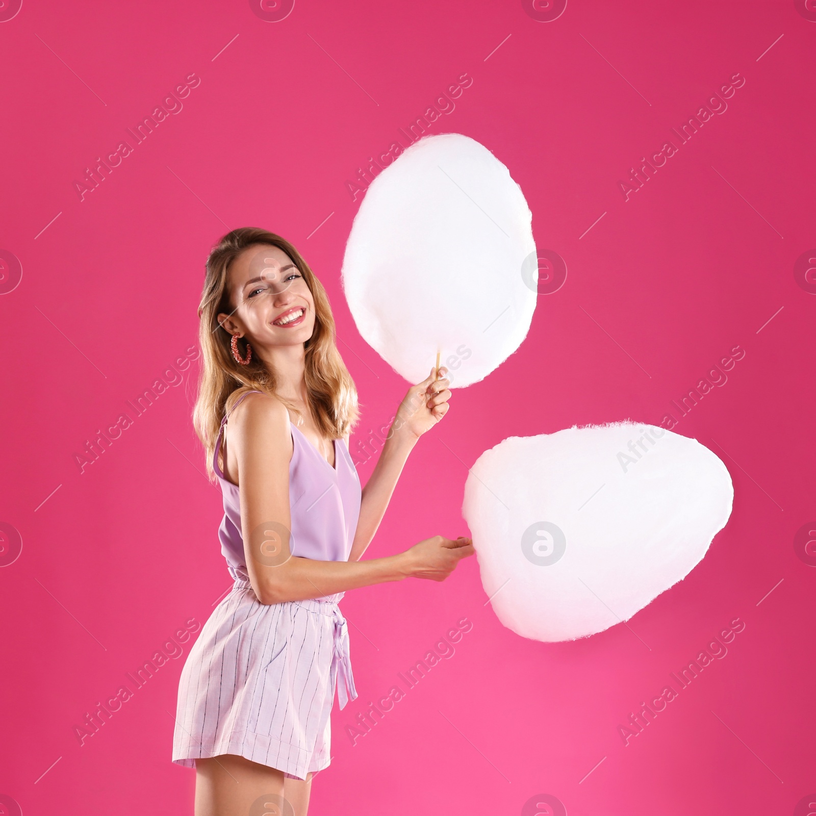 Photo of Happy young woman with cotton candies on pink background