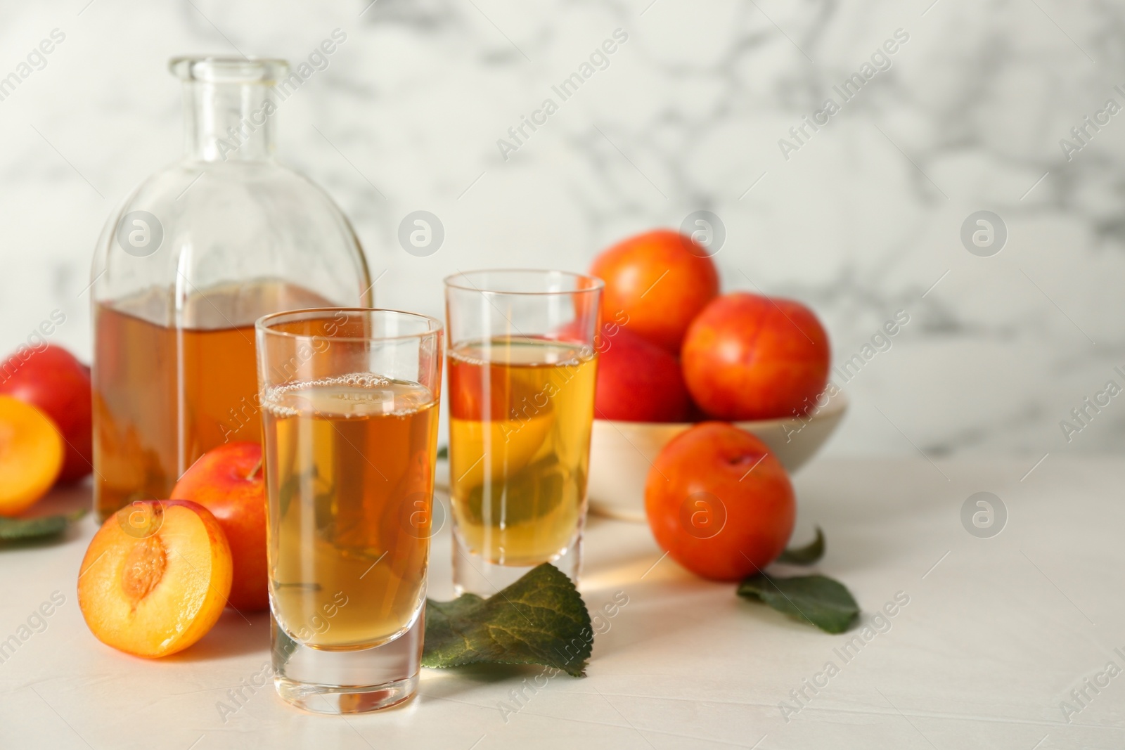 Photo of Delicious plum liquor and ripe fruits on white table. Homemade strong alcoholic beverage