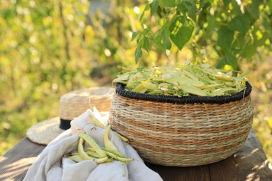 Wicker basket with fresh green beans on wooden table in garden