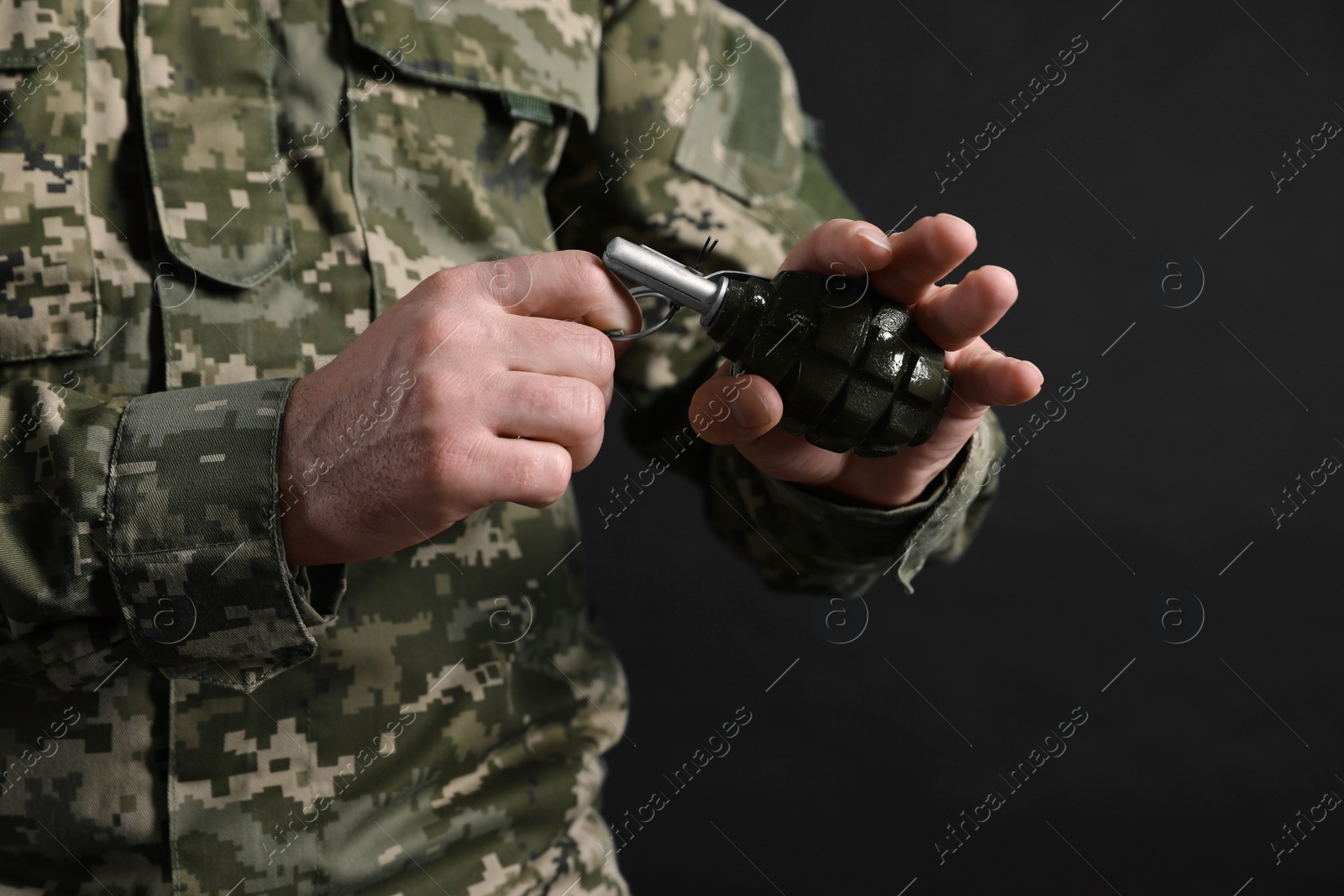 Photo of Soldier pulling safety pin out of hand grenade on black background, closeup. Military service