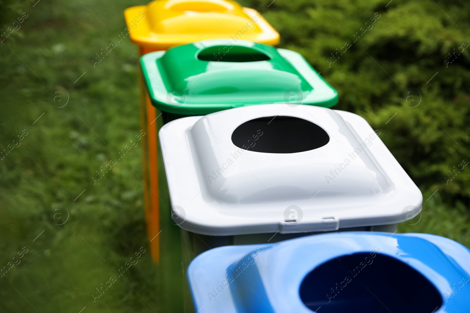 Photo of Many color recycling bins on green grass outdoors, closeup. Space for text