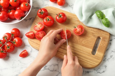 Top view of woman cutting fresh cherry tomatoes on board at table, closeup