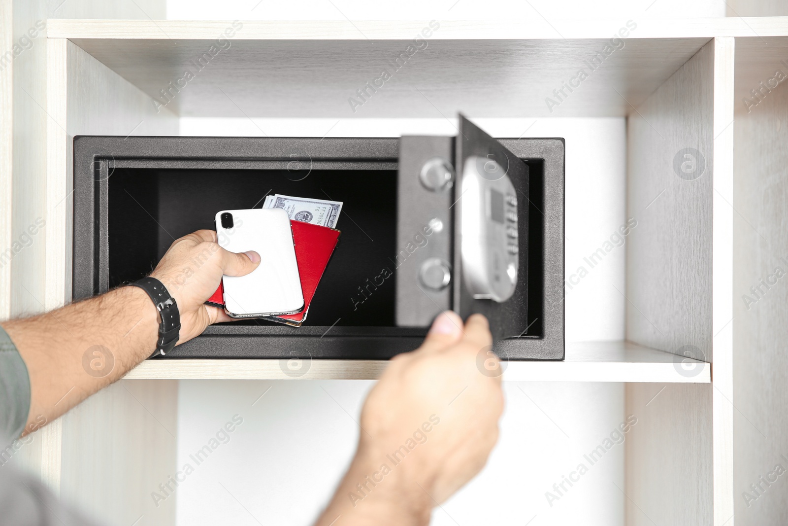 Photo of Man putting smartphone, passport and money into steel safe, closeup