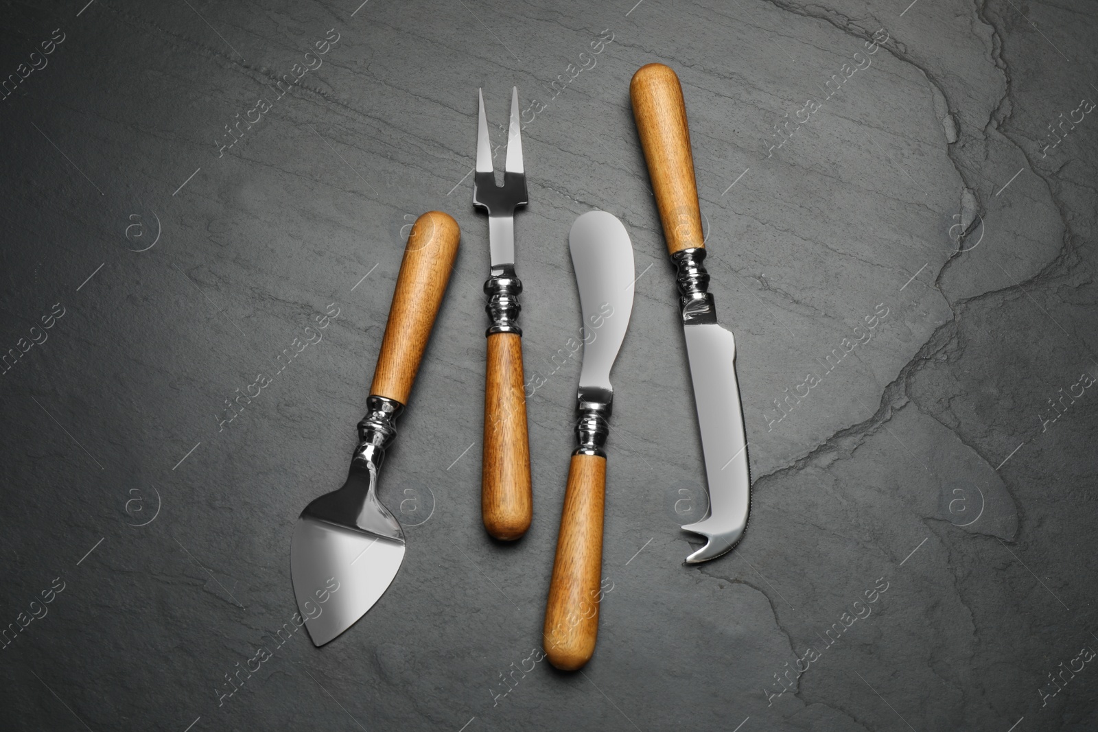 Photo of Cheese knives and fork on black stone table, flat lay