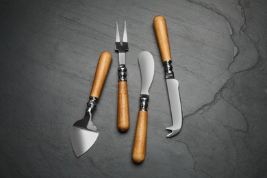 Photo of Cheese knives and fork on black stone table, flat lay