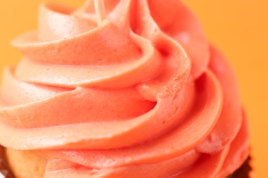 Photo of Delicious cupcake with bright cream on orange background, closeup