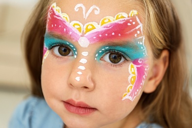 Photo of Cute little girl with face painting indoors, closeup