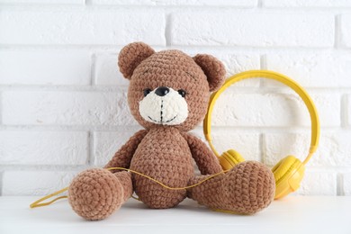 Photo of Baby songs. Toy bear and yellow headphones on white wooden table