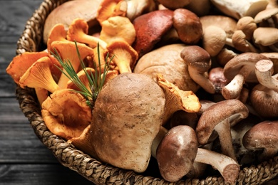 Photo of Different fresh wild mushrooms in wicker bowl on table, closeup