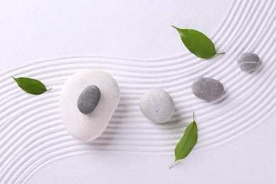 Photo of Zen garden stones and green leaves on white sand with pattern, flat lay