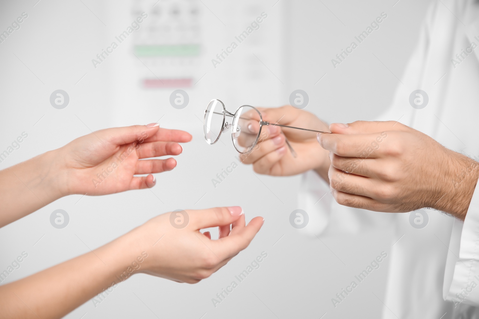 Photo of Male ophthalmologist helping woman choose glasses in clinic, closeup